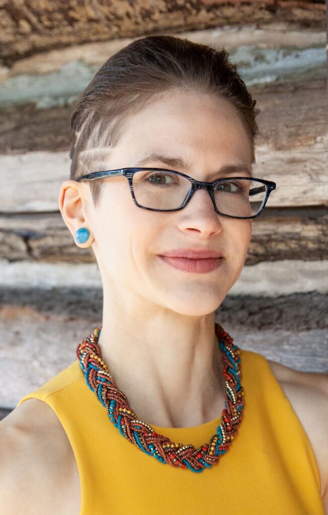 A headshot of a white woman with short hair and glasses.